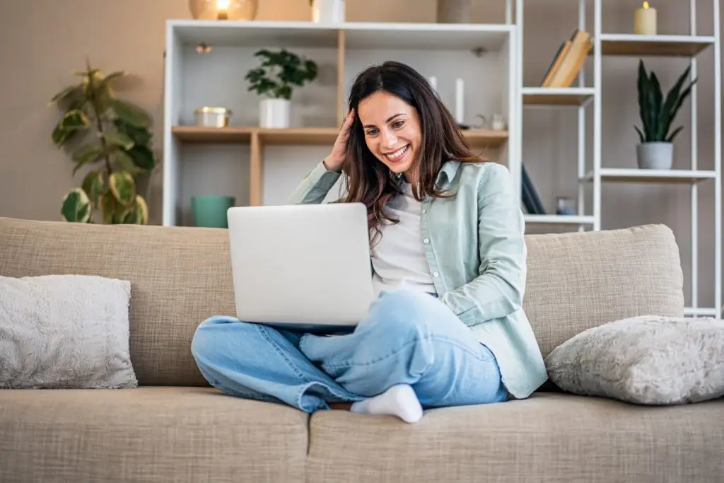 Woman smiling using laptop on living room couch